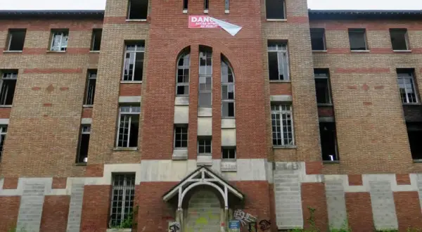 Façade imposante de l'hôpital abandonné d'Angicourt, avec ses fenêtres brisées et un panneau "DANGER ACCÈS INTERDIT AU PUBLIC".