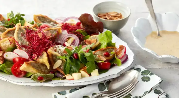 Herzhafter Maultaschen Salat mit knackigem Gemüse, roten Zwiebeln, Granatapfelkernen und Mandelsplittern. Dazu eine cremige Sauce.