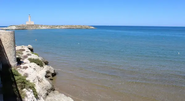 Faro di Vieste, Stella Maris, su un'isola rocciosa con mare azzurro e spiaggia sabbiosa.