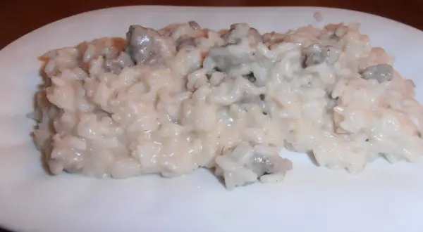 Un cremoso risotto salsiccia e patate, servito su un piatto bianco.