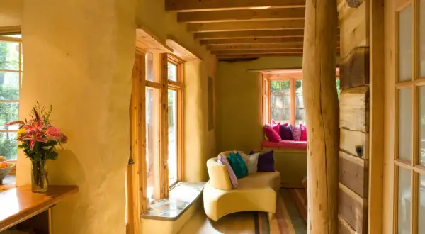 Interno accogliente con pareti in intonaco terra cruda, mobili in legno grezzo e un divano giallo con cuscini colorati.