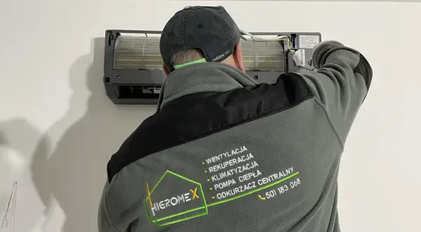 Technik w czapce z daszkiem montuje jednostkę klimatyzacyjną.