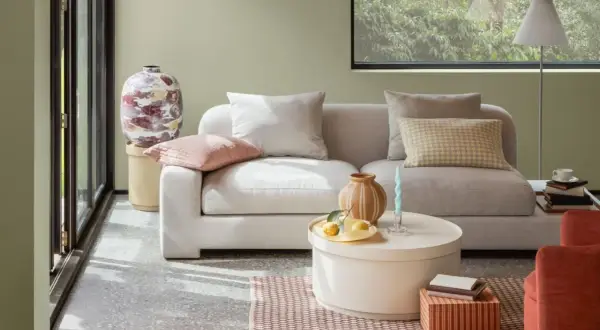 Gemütliches Wohnzimmer mit hellgrauem Sofa, Kissen in sanften sommer farben und einem runden Couchtisch.