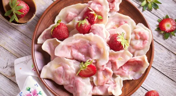 Pyszne pierogi z truskawkami, udekorowane świeżymi owocami, na glinianym talerzu.