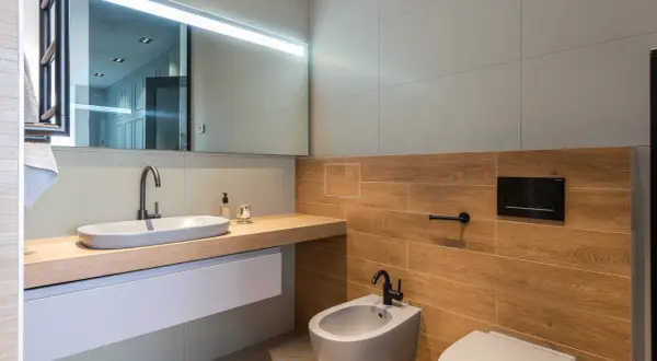 Bagno moderno con lavabo ovale, bidet e WC. Le pareti sono rivestite con piastrelle effetto legno e grigie, un mix che offre ottime opinioni per chi ama il design.
