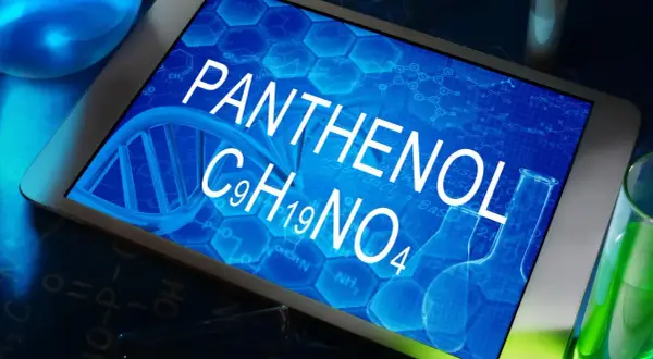 Tablet z napisem PANTHENOL i wzorem chemicznym C9H19NO4, otoczony probówkami z zielonym płynem i elementami chemicznymi.