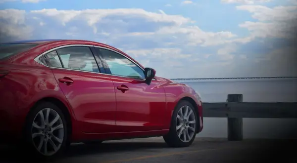 Czerwona Mazda 6 2.0 benzyna zaparkowana nad wodą, z mostem w tle.