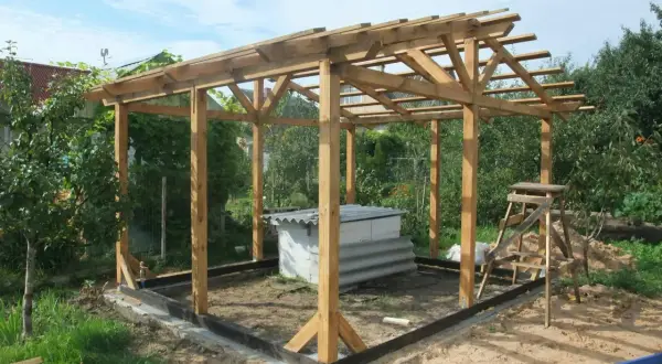 Drewniana konstrukcja altany w trakcie budowy, z widocznym fundamentem i dachem.