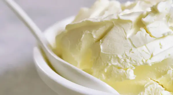 Kremowa masa w białej miseczce z łyżką. Szukasz, czym zastąpić mascarpone? Oto puszysta alternatywa.