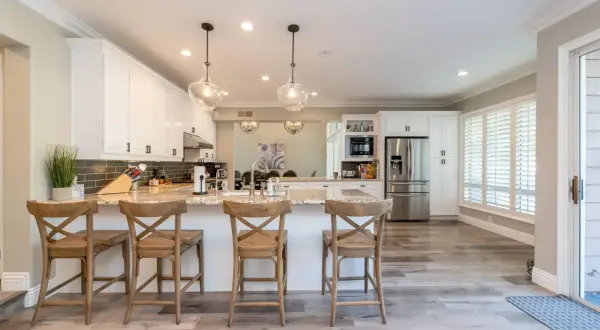 Cocinas abiertas al salón pequeñas con isla central, taburetes de madera y electrodomésticos modernos.