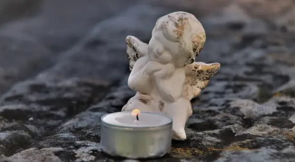 Aniołek czuwa przy płonącej świecy, symbolizując pamięć i żal po śmierci bliskiej osoby.