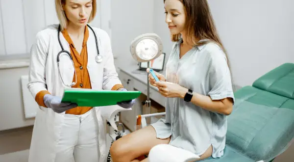 Lekarka wyjaśnia pacjentce, czy można robić cytologię podczas okresu. Pacjentka trzyma w dłoni niebieskie narzędzie.