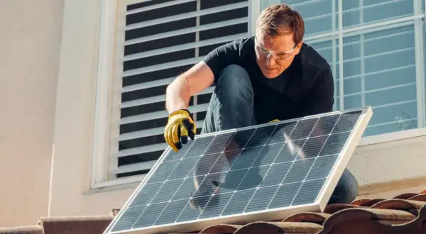 Mężczyzna w okularach ochronnych montuje panel słoneczny na dachu, walcząc ze zmianami klimatycznymi.
