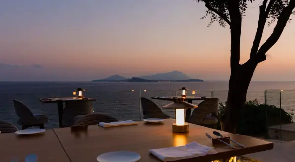 Tavoli apparecchiati con vista mare al tramonto, un'atmosfera magica che fa pensare ai migliori ristoranti di Napoli.