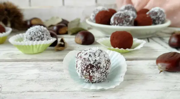 Deliziosi tartufini di castagne, alcuni ricoperti di cocco, altri di cacao, su un tavolo di legno con castagne sparse.