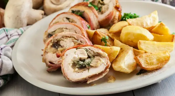 Roladki z kurczaka zawinięte w boczek, podane z pieczonymi ziemniakami i ziołami.