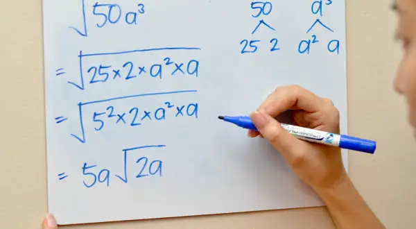 Eine Hand schreibt auf einem Whiteboard, wie man die Wurzel umschreibt: $\sqrt{50a^3}$ wird zu $5a\sqrt{2a}$ vereinfacht.