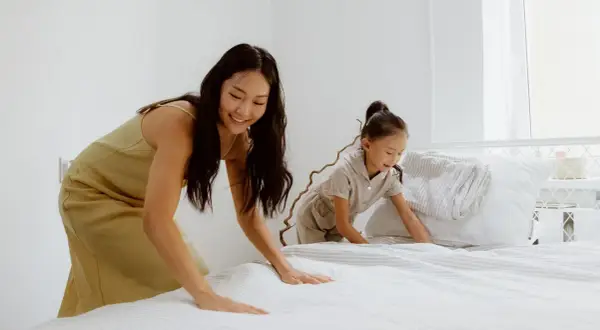 Mutter und Kind machen das Bett frisch. Der Boxspringbett Topper wellt sich leicht, während sie die Bettwäsche glattziehen.