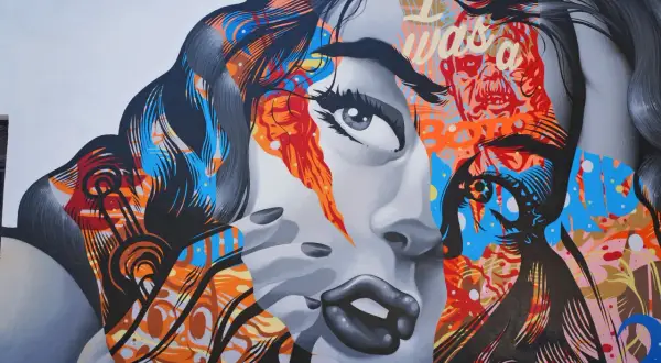 Mural z twarzą kobiety, pełen jaskrawych kolorów i abstrakcyjnych wzorów, oddaje dynamikę i wyrazistość cech pop artu.