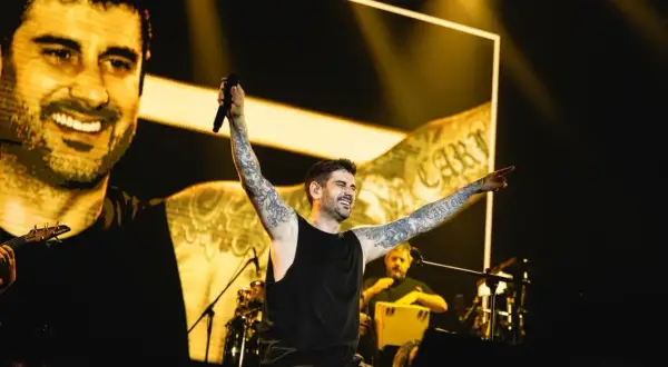 Melendi en concierto en Zaragoza, con los brazos en alto y sonriendo, ante una multitud.