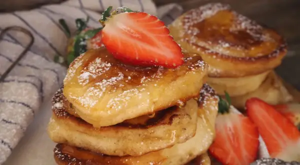 En stapel fluffiga pannkakor på filmjölk, toppade med färska jordgubbar och pudersocker.