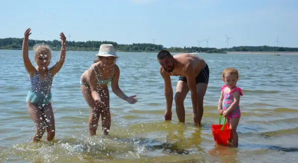 Rodzina pluska się w wodzie na zalewie Cieszanowice. Dzieci radośnie chlapią, a ojciec dogląda zabawy.