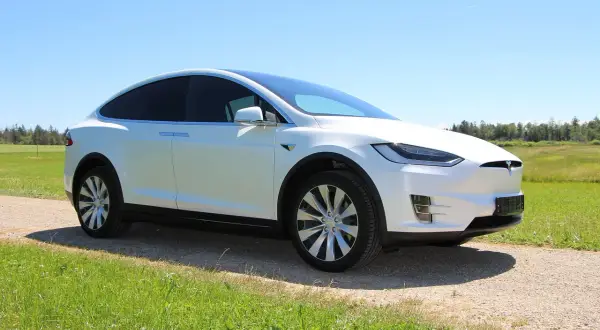 Biała Tesla Model X na tle zielonej łąki i lasu. Zastanawiasz się, ile kosztuje Tesla?