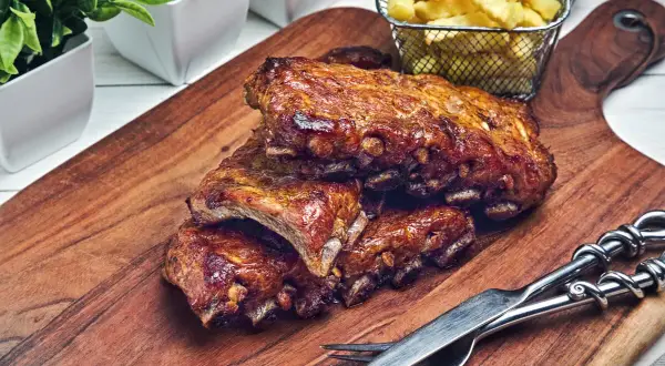 Saftige, geschmorte Rippchen mit knusprigen Pommes Frites auf einem Holzbrett, bereit zum Genießen.