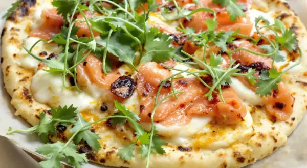 Pizza saumon avec fromage fondant, garnie de coriandre fraîche et d'une touche de piment. Un délice visuel et gustatif.