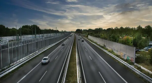 Szeroka autostrada A2 z ruchem samochodowym, otoczona zielenią i ekranami akustycznymi.
