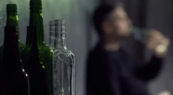 Puste butelki, jedna z nich jest przezroczysta, a obok niewyraźna postać pije alkohol. To może być jego dawka śmiertelna.
