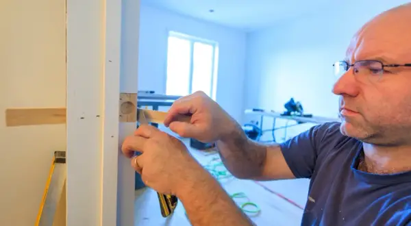 Un homme ajuste un bloc-porte sur un mur existant. Il utilise un outil pour s'assurer de la bonne pose.