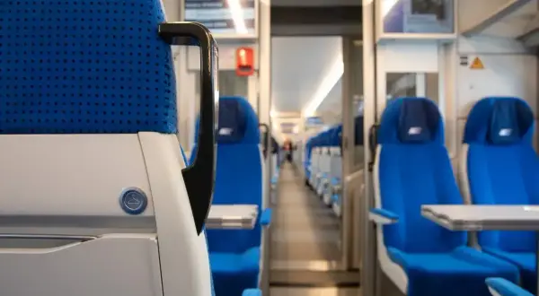 Wnętrze pociągu sypialnego z rzędami niebieskich siedzeń i stolikami.