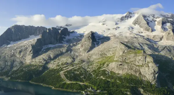 Majestätischer Marmolada Gletscher, umgeben von felsigen Gipfeln und grünen Hängen, mit einem See im Vordergrund.