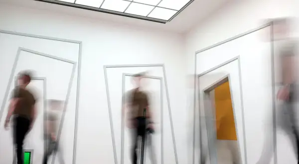 Mensen bewegen door een gang met geometrische openingen, wat een indruk geeft van een sensorische informatieverwerking test.