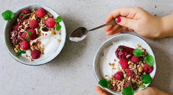 Två skålar med kokosyoghurt, hallon, granola och mynta. Perfekt för ett enkelt kokosyoghurt recept.