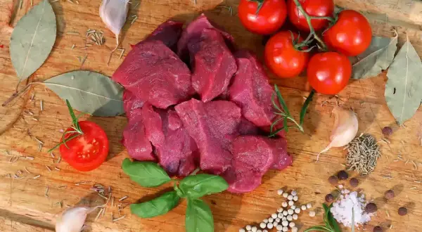 Surowe, pokrojone w kostkę mięso wołowe, pomidory, czosnek, liście laurowe i zioła na desce do krojenia. Idealne składniki, jakie mięso na gulasz.
