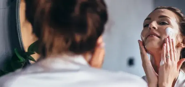 Frau trägt Schaum auf ihr Gesicht auf. Sie fragt sich: "Allantoin, was ist das?" Es ist ein beruhigender Inhaltsstoff für die Haut.