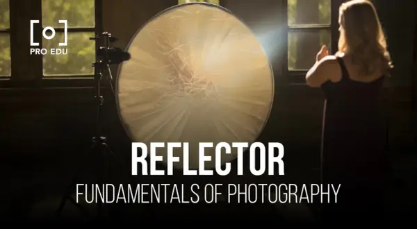 A large, round reflector is used to bounce light in this photography setup. A woman stands in the background, her hands raised.