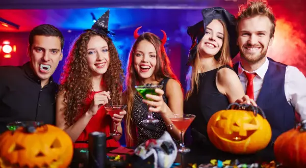 Glada vänner firar halloween med drinkar och pumpor. Perfekt för halloween lekar vuxna!