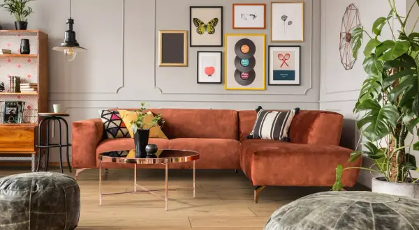 Pomarańczowa kanapa i stolik kawowy w stylu mid century modern. Na ścianie galeria obrazów z motywami retro.