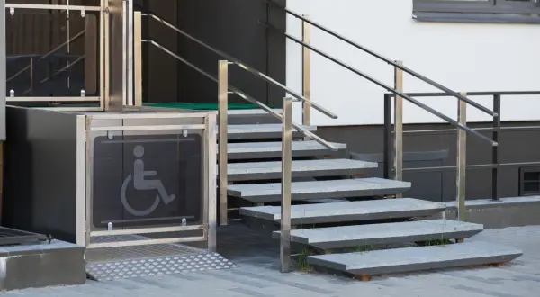 Un montascale con simbolo disabili, accanto a una scala esterna in metallo. La manutenzione è fondamentale per garantire l'accessibilità.