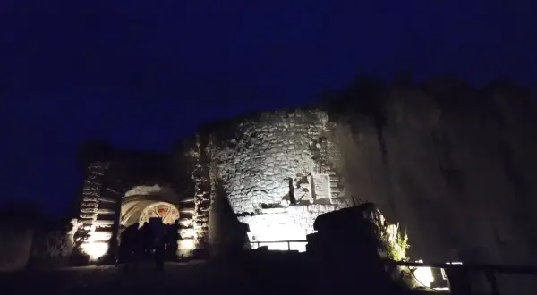 Nuit tombante sur un château abandonné dans la Somme. Des lumières éclairent l'entrée voûtée et les vieilles pierres.