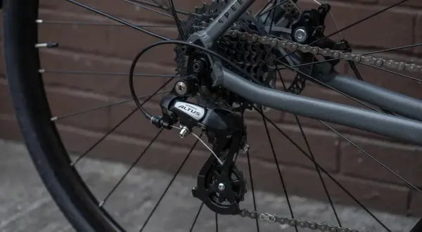 Tylna przerzutka Shimano Altus z widocznym hakiem do przerzutki, kasetą i łańcuchem na rowerze.