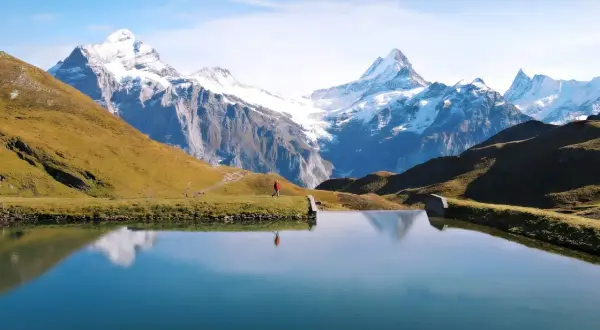 Osoba w czerwonej kurtce spaceruje nad jeziorem w Grindelwald, podziwiając ośnieżone szczyty Alp.