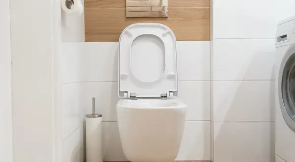 Cassetta a muro WC perde acqua, un problema comune in bagno. Si vede il water sospeso, il rotolo di carta igienica e la lavatrice.