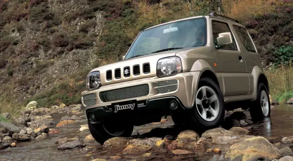 Złoty Suzuki Jimny (1998) pokonuje kamienisty strumień, gotowy na każdą przygodę.