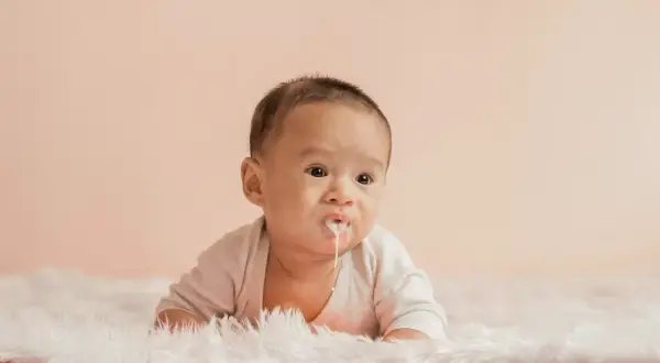 Söt bebis med mjölk runt munnen, kanske lite reflux bebis. Ligger på en fluffig matta.