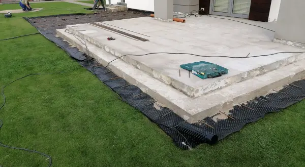 Budowa tarasu z betonu. Pracownicy przygotowują teren pod nową nawierzchnię, układając zbrojenie i materiały izolacyjne.