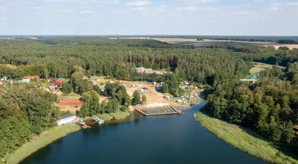 Widok z lotu ptaka na jezioro, plażę z ludźmi, kemping i las. Sprawdź jezioro przechlewskie cennik na wakacje.